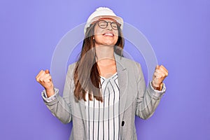 Professional woman engineer wearing industrial safety helmet over pruple background very happy and excited doing winner gesture