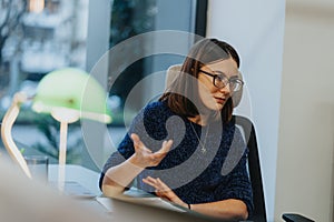 Professional woman in glasses engaged in business discussion at office desk.