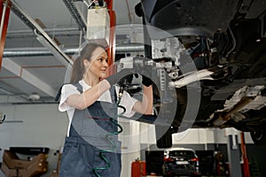Professional woman mechanic fixing disc brake with drill doing wheel replacement