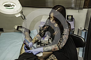Professional woman tattooer working tattoo in a man leg. High an photo