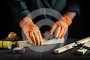 Professional woodworker cleans wooden plank with abrasive tools. Hands of the builder close-up during work. Renovation or