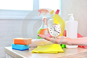 Professional worker from cleaning company holds a clock in her hand under the household chemicals.