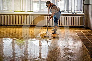 Professional worker lacquering old parquet floors using roller. Floor renovation