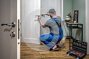 Professional worker locksmith in uniform installing, working with house door lock using screwdriver