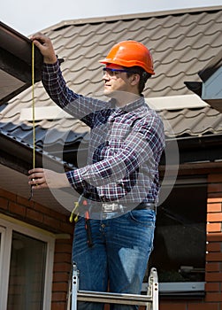 Professional worker measuring height of roof with tape