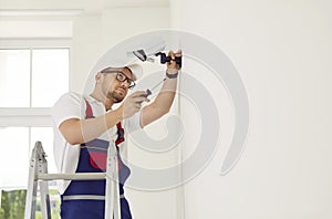 A professional worker standing on a stepladder installs a video surveillance camera on the wall.