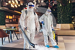 Professional workers in hazmat suits disinfecting indoor of cafe or restaurant, pandemic health risk, coronavirus