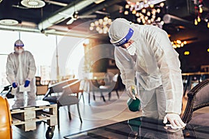 Professional workers in hazmat suits disinfecting indoor of cafe or restaurant, pandemic health risk, coronavirus photo