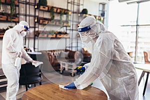 Professional workers in hazmat suits disinfecting indoor of cafe or restaurant, pandemic health risk, coronavirus