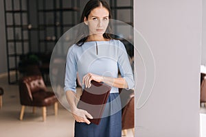 Professional young business woman holding file folder while standing near window in modern office.