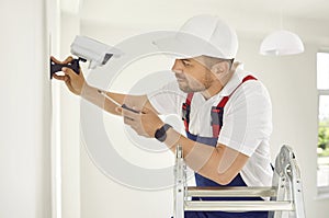 Electrician worker installs and screws surveillance video camera on wall in bright office space.