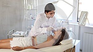 Professional young female cosmetologist performing facial radiofrequency procedure on woman stimulating collagen