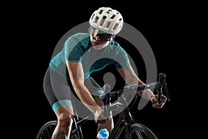 Professional young female cycler on road bike isolated over black studio background.