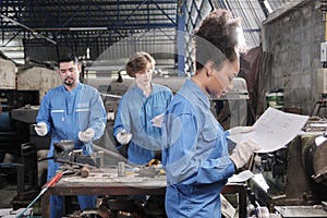 Professional young female worker with team in metalwork manufacturing factory