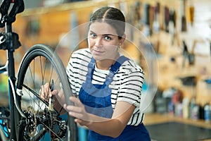 Professional young girl master wearing uniform fixing bike, lubricating bicycle chain in sport store photo