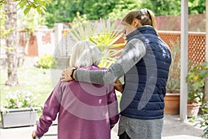 Professional young helpful caregiver walking with the elderly woman in the garden at nursing home. Elderly care concept