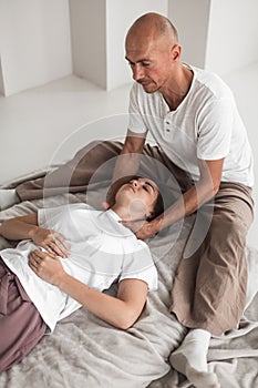 Professional young man massaging a woman& x27;s neck in a white cozy room during a manual therapy