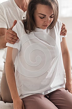 Professional young man massaging a woman& x27;s shoulders in a white cozy room during  manual therapy
