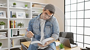 A professional young man multitasking in a modern office, talking on the phone while taking notes