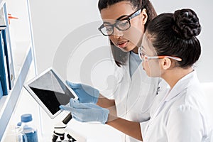Professional young scientists using digital tablet while making experiment in chemical laboratory