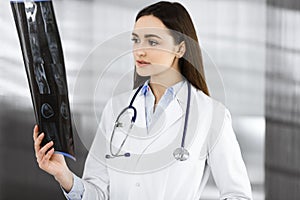 Professional young woman-doctor is looking at her patient& x27;s roentgenogram. Physician at work in a clinic& x27;s office