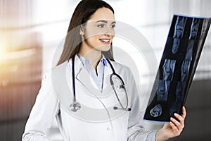 Professional young woman-doctor is looking at her patient& x27;s roentgenogram. Physician at work in sunny clinic photo