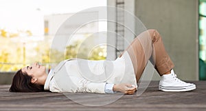 A professional young woman in smart casual attire with a beige blazer and brown trousers relaxes outdoors