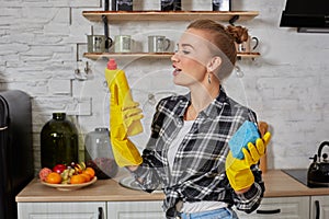 Professional young woman wearing rubber protective yellow gloves holding bottle cleaners in the kitchen.