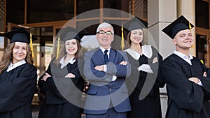 A professor and his students in graduation gowns stand with their arms crossed over their chests.