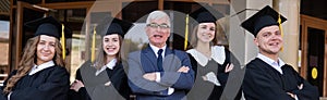 A professor and his students in graduation gowns stand with their arms crossed over their chests.