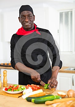 Proffesional male cook in black uniform chopping vegetables
