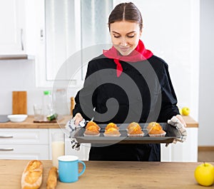 Proffesional woman in chef uniform holding sheet pan with just baked cupcakes