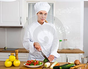 Proffesional woman cook in white uniform chopping vegetables