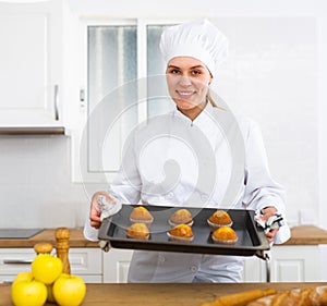 Proffesional woman cook in white uniform holding sheet pan with just baked cupcakes