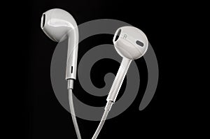 Proffessional close up of white earbuds isolated agains black background with rim lighting from sides.