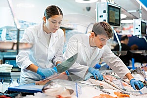 Proficient sellers cutting piece of tuna on tabletop in fish store