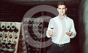 Proficient smiling man holding glass of wine in cellar