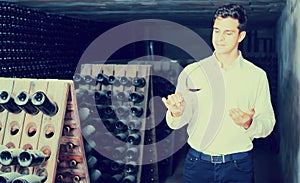 Proficient young man holding glass of wine in cellar