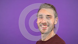 Profil portrait of attractive long-haired man smiling over isolated purple background. the man is wearing a burgundy