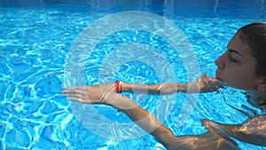 Profile of attractive woman swimming in pool with blue clear water in warm summer day. Young girl relaxing during summer