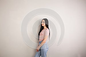 Profile of attractive young brunette woman with long hair standing by the grey background wearing pink shirt and jeans