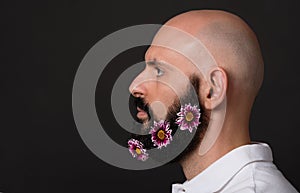 Profile of bald unshaven man with beard with chrysanthemum flowers on dark background