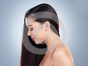 Profile of a beautiful young brunette woman with healthy hair and skin posing against a grey studio background. Young