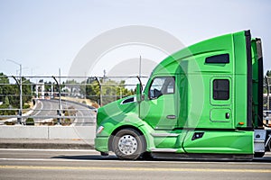 Profile of the big rig green semi truck with sleeping cab compartment running on the bridge overpass the highway road