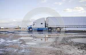 Profile of big rig semi truck with refrigerator semi trailer standing on unequipped parking lot with industrial equipment and