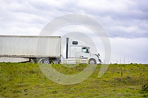 Profile of big rig semi truck transporting cargo in dry van semi trailer running on the road on the top of the hill