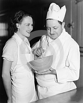 Profile of a chef stirring a mixture in a bowl and a young woman standing beside him