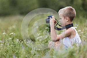 Profile close-up portrait of young blond cute handsome child boy with camera taking pictures outdoors on bright sunny spring or