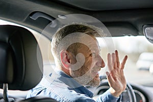 Profile of a friendly car driver with graying hair and beard greeting someone with his hand