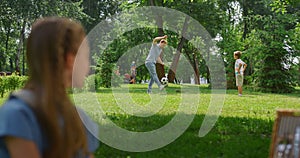 Profile girl watching soccer game in park. Father play football with son.